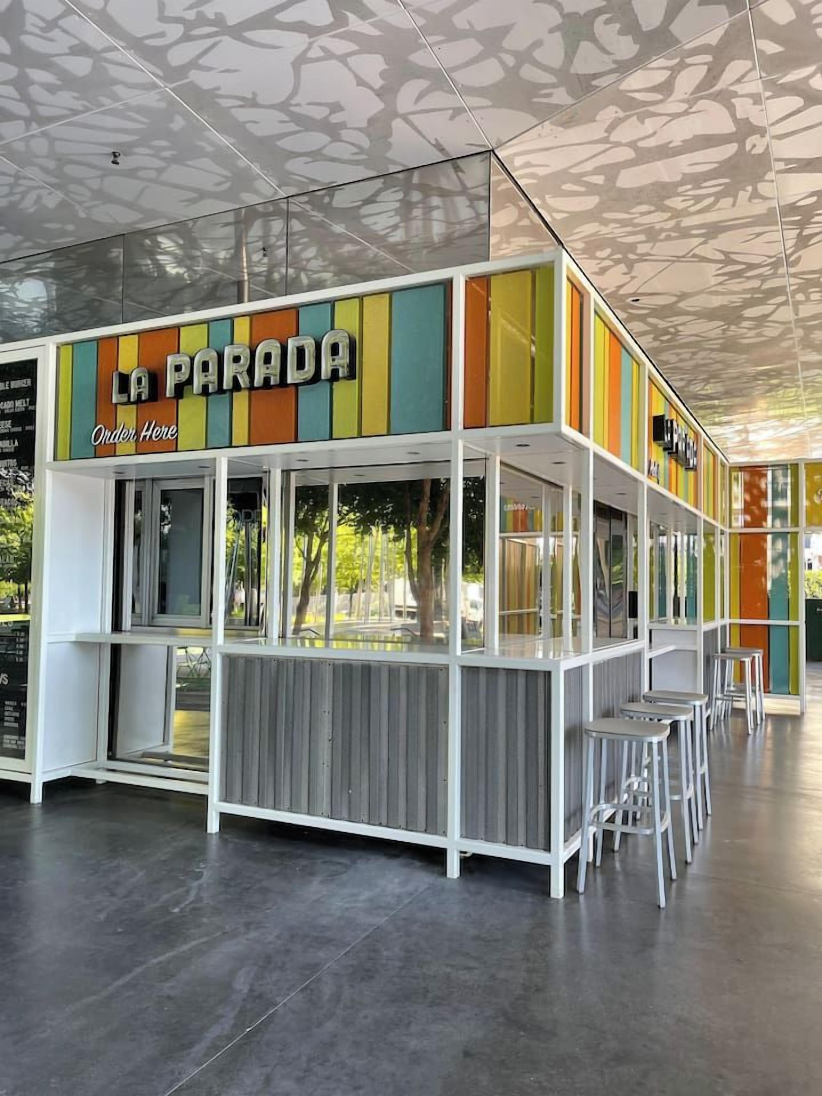 A food kiosk named 'La Parada' with a colorful vertical design, a counter, and bar stools.