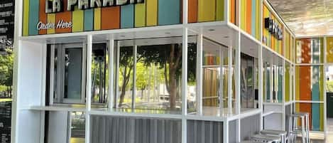A food kiosk named 'La Parada' with a colorful vertical design, a counter, and bar stools.