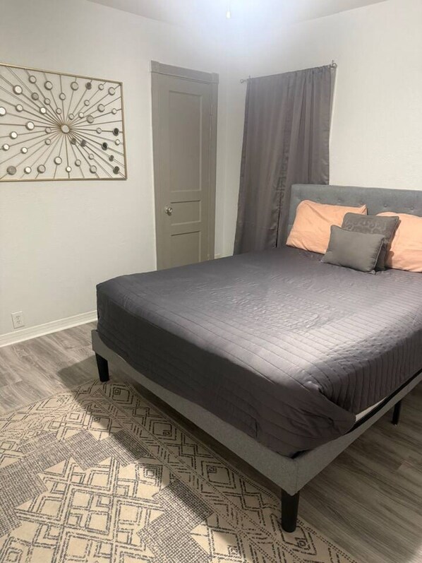 A bedroom with a bed, a patterned rug, a door, and a wall decoration.