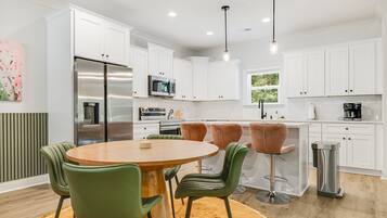 Una cocina moderna con armarios blancos, electrodomésticos de acero inoxidable y una mesa de comedor redonda con sillas verdes.
