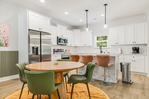 Une cuisine moderne avec des meubles blancs, des appareils en acier inoxydable et une table de salle à manger ronde entourée de chaises vertes.