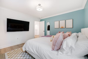 A bedroom with a bed, a flat-screen TV mounted on the wall, a mirror, and three framed artworks. - Hot tub, Mini golf, Fire pit, Game room, Sleeps 14 (Charlotte)