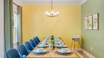 Un comedor con una larga mesa dispuesta para una comida, sillas azules, una araña de cristal y una trona para bebés.