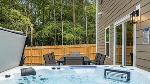 A hot tub with a table and chairs in a backyard with a wooden fence and trees. - Hot tub, Mini golf, Fire pit, Game room, Sleeps 14 (Charlotte)