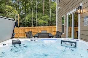 A hot tub with a table and chairs in a backyard with a wooden fence and trees. - Hot tub, Mini golf, Fire pit, Game room, Sleeps 14 (Charlotte)