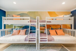 Une chambre avec un lit superposé, une échelle, des oreillers et une fresque murale colorée.