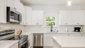 A modern kitchen with white cabinetry, stainless steel appliances, a dishwasher, and a coffee maker. - Hot tub, Mini golf, Fire pit, Game room, Sleeps 14 (Charlotte)