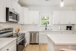 A modern kitchen with white cabinetry, stainless steel appliances, a dishwasher, and a coffee maker. - Hot tub, Mini golf, Fire pit, Game room, Sleeps 14 (Charlotte)