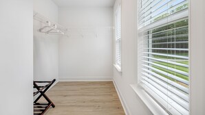 A room with a wooden floor, white walls, a window with blinds, and a clothes drying rack. - Hot tub, Mini golf, Fire pit, Game room, Sleeps 14 (Charlotte)