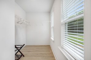 A room with a wooden floor, white walls, a window with blinds, and a clothes drying rack. - Hot tub, Mini golf, Fire pit, Game room, Sleeps 14 (Charlotte)