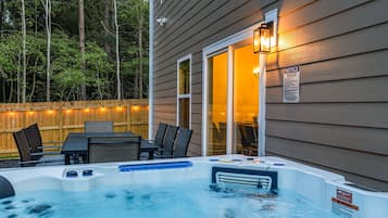 Un jacuzzi con un muelle de madera y sillas, una valla de madera y una casa con una ventana iluminada.
