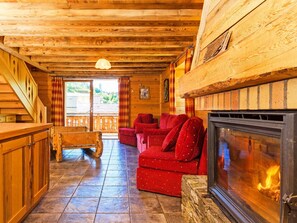 A cozy log cabin interior with a fireplace, red upholstered furniture, and a wooden staircase.