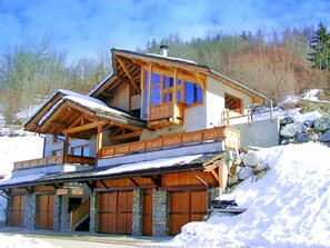 Una cabaña de madera de varios pisos con balcón y cimientos de piedra, rodeada de nieve.