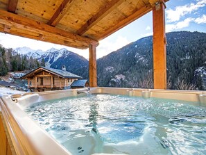 A hot tub with a wooden structure overhead, surrounded by a mountainous landscape and a lodge. - Balcon du Paradis by Interhome (Peisey-Nancroix)