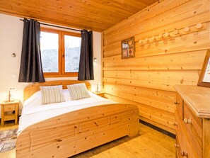 Un dormitorio de cabaña de madera con cama, mesita de noche, cómoda y ventana con cortinas.