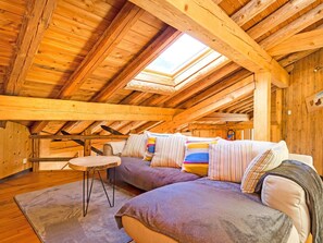 Una habitación cálida en el ático, con techo inclinado, vigas de madera, un conjunto de sofás, una pequeña mesa redonda y un tragaluz.