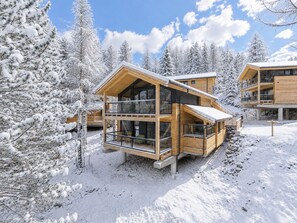A wooden chalet with a balcony and large windows, surrounded by snow-covered trees. - 02_NTH054_18e_Sup Chalet mit Sauna und Hot Tub 2 E by Interhome (Großveitsch)