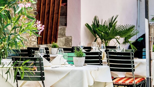 An outdoor dining area with tables set for two, surrounded by potted plants and a stone wall. - Auberge Adler, (Fläsch). Doppelzimmer by Interhome (Fläsch)