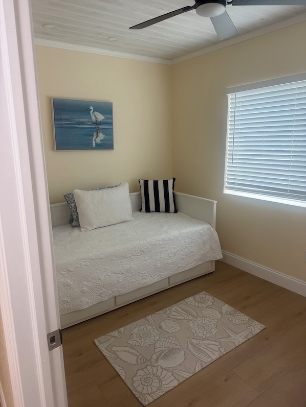 Een slaapkamer met een bed, een plafondventilator, een raam met zonwering en een schilderij aan de muur.