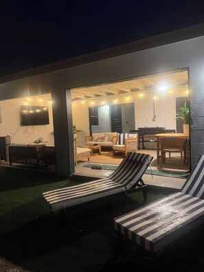 An outdoor living area with a pool, lounge chairs, a dining table, and a kitchen visible through an open door. - Coastal Haven Getaway (Treasure Island)