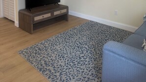 Habitació amb ventilador de sostre, televisió sobre un suport de fusta, una catifa amb dibuixos i un sofà.