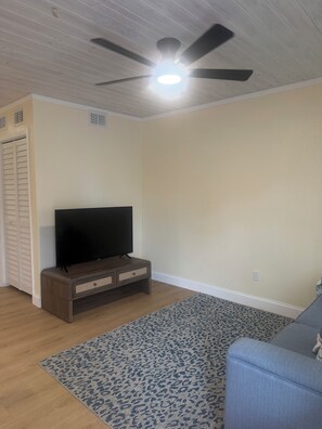 A room with a ceiling fan, a television on a wooden stand, a patterned rug, and a couch. - Coastal Haven Getaway (Treasure Island)