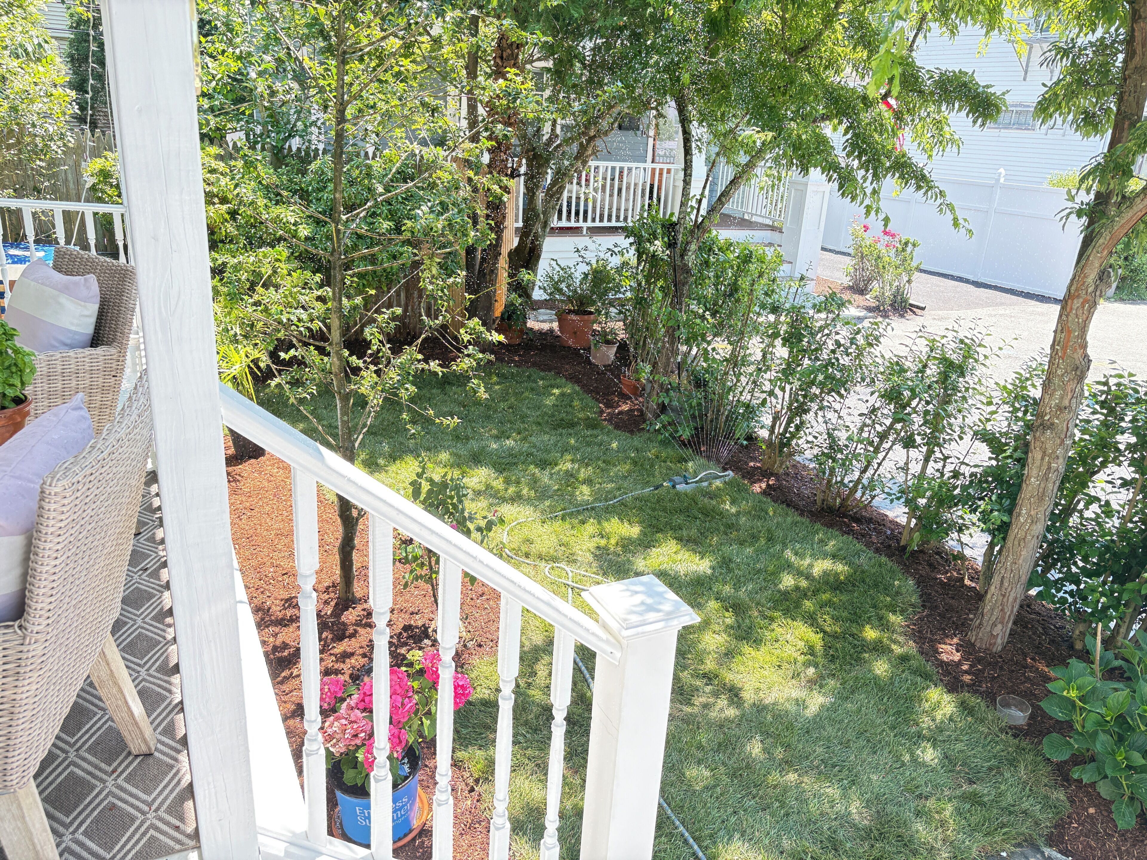 Un patio trasero con cerca blanca, césped y varios maceteros con plantas.