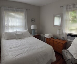 Ein Schlafzimmer mit einem großen Bett, zwei Nachttischen, einem Schminktisch und einem Heizkörper, sowie einem Fenster mit Jalousien.