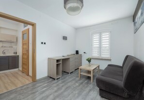 A modern living room with a grey sofa, a wooden coffee table, and a kitchen area with a wooden cabinet and a built-in oven.