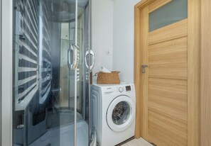 A laundry room with a washing machine, a wooden door, and a glass door leading to a shower area.