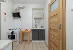A compact kitchen with a stove, a sink, and a small table with cups and grapes.