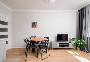 A modern living room with a round wooden table, black chairs, a flat-screen TV, a grey cabinet, and a potted plant. - Wola Ratusz Comfort Apartment (Warszawa)