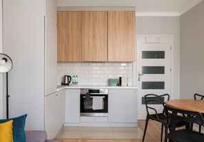A compact kitchen with wooden cabinets, a white countertop, and a small oven. - Wola Ratusz Comfort Apartment (Warszawa)