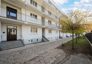 A multi-story residential building with a paved walkway, a tree, and a parked car. - Wola Ratusz Comfort Apartment (Warszawa)