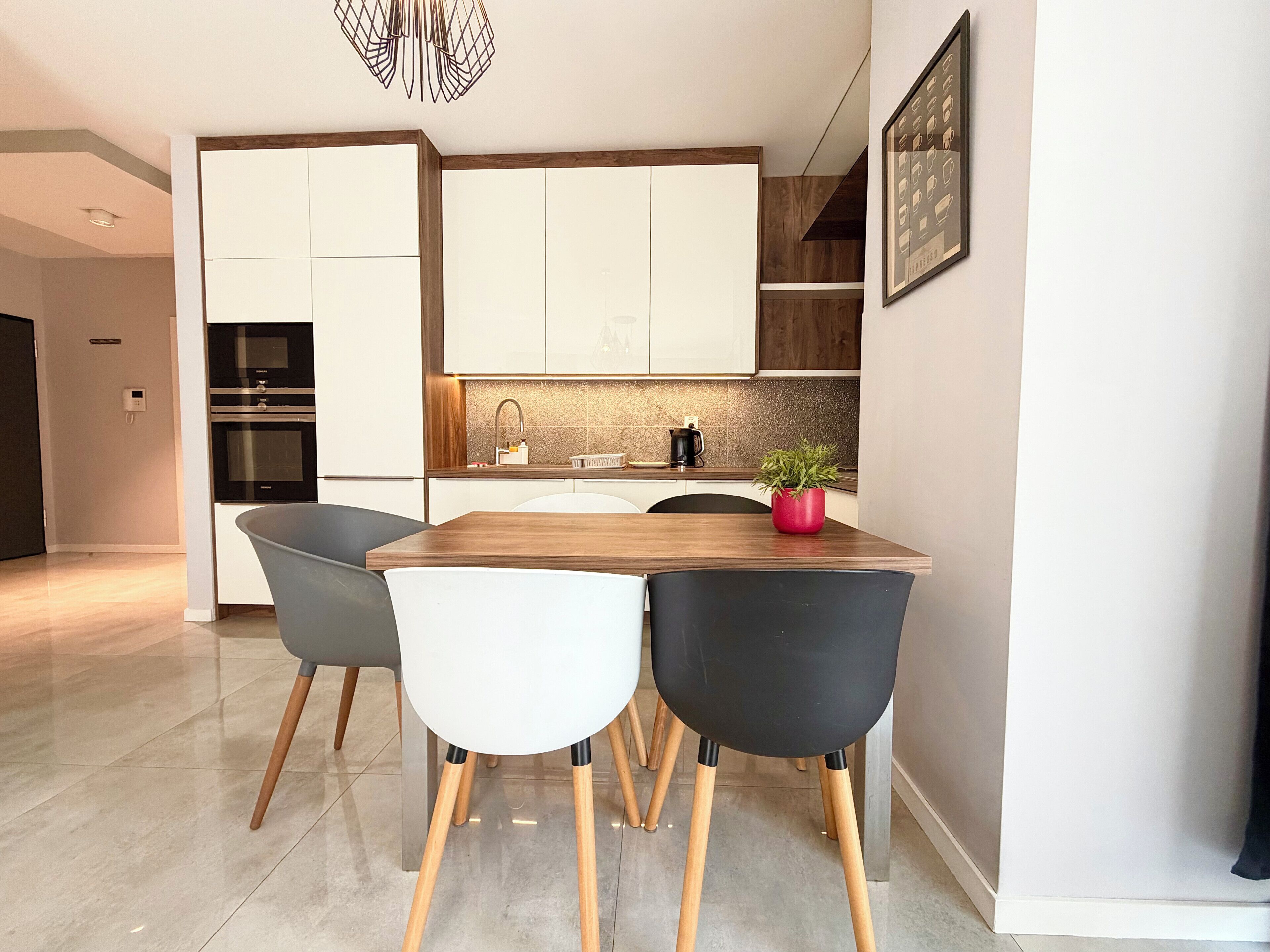 A modern kitchen with white cabinets, a wooden dining table, and two chairs.