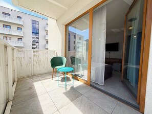 A balcony with a chair and table, a sliding glass door leading to a room with a bed, and a view of other buildings. - Bulwary Książęce Central Apartment (Wrocław)