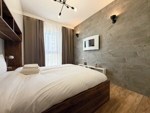 A modern bedroom with a large bed, a mounted TV, and a stone wall. - Bulwary Książęce Central Apartment (Wrocław)