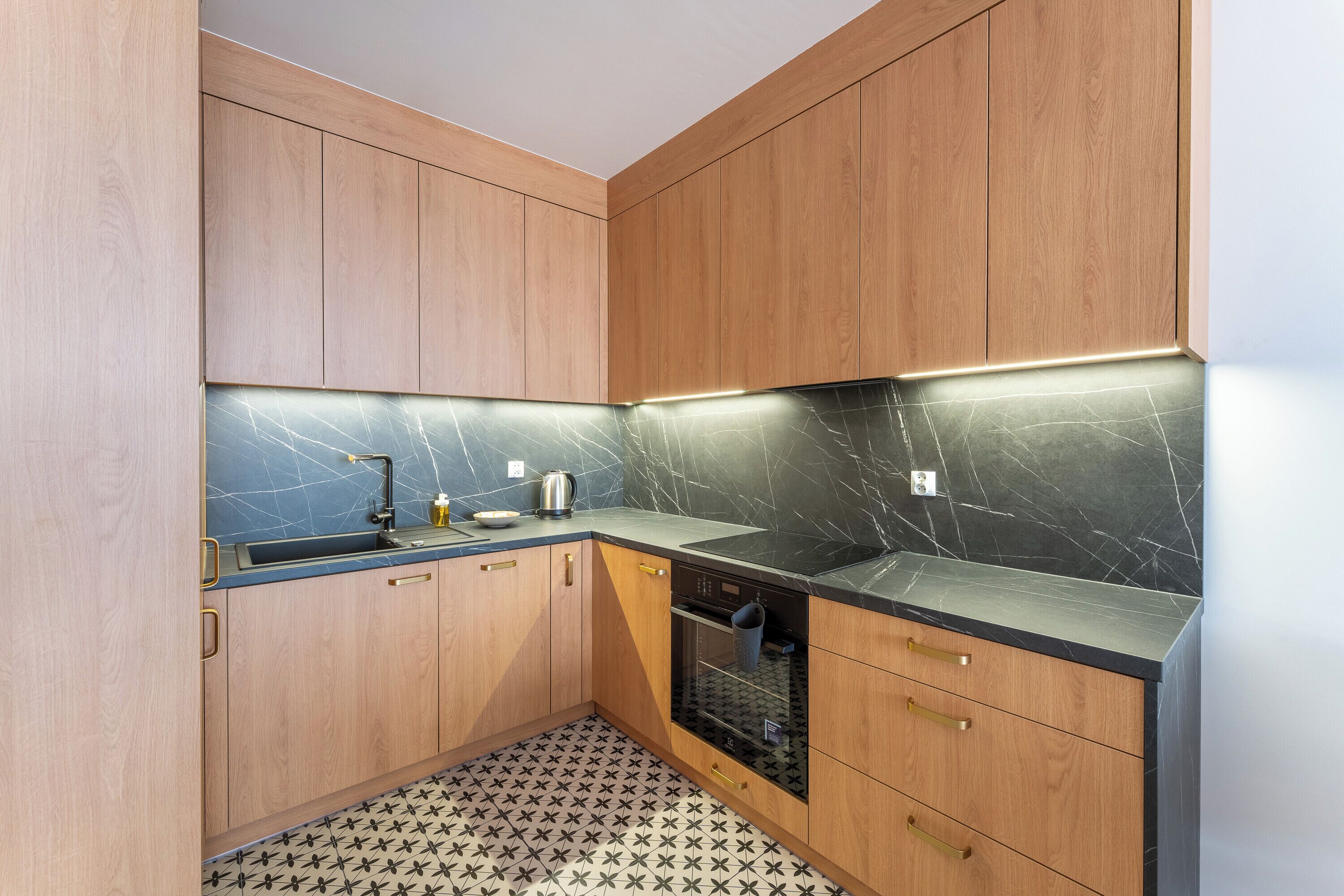 A compact kitchen with wooden cabinets, a black countertop, and a patterned floor.