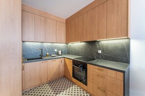 A compact kitchen with wooden cabinets, a black countertop, and a patterned floor. - Koszalińska Harmony Apartment (Kołobrzeg)