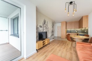 Ein modernes Wohnzimmer mit Fernseher, Holzmöbeln und einem Essbereich mit Küche im Hintergrund.
