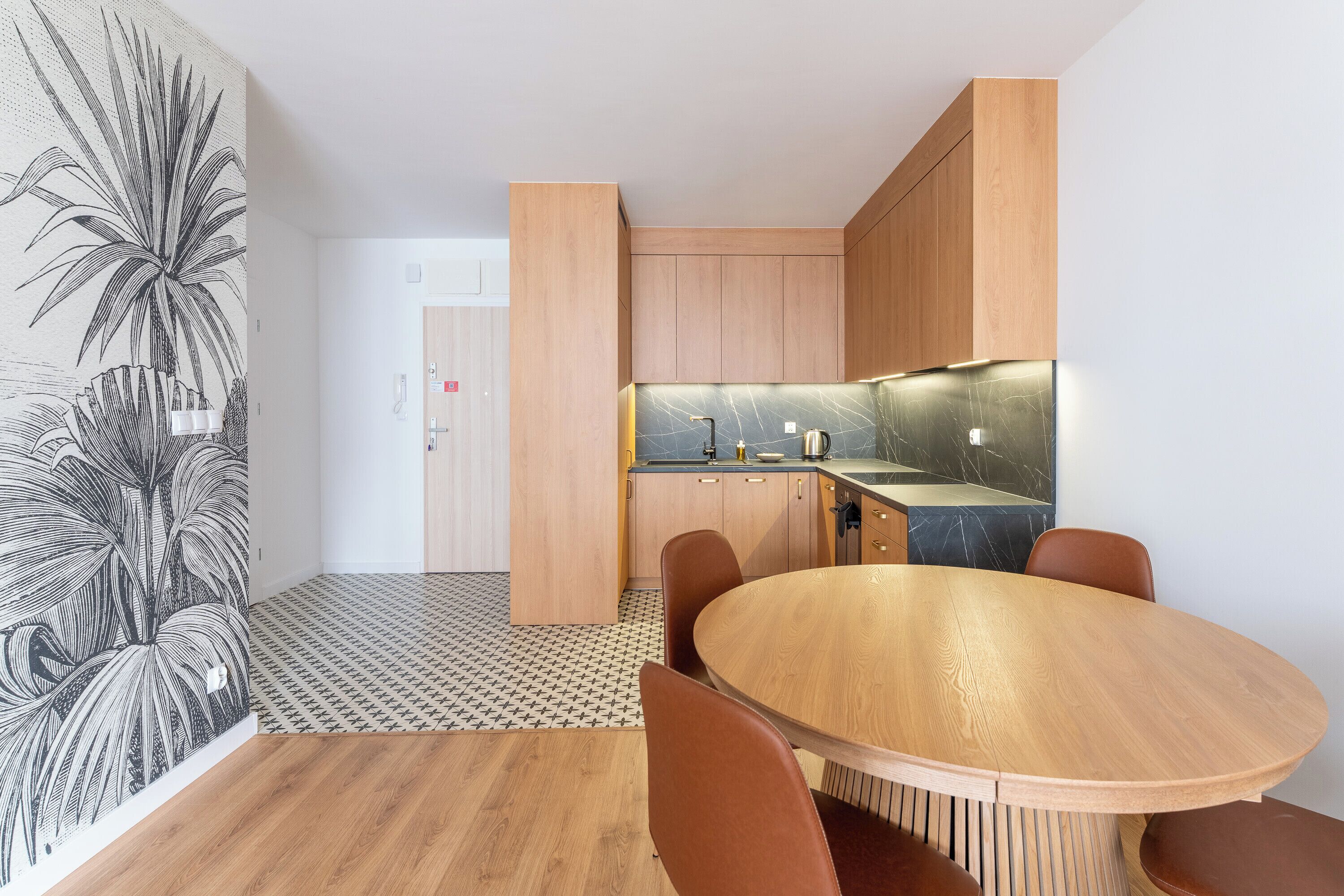 Una cocina moderna con armarios de madera, encimera de mármol y comedor con mesa y sillas de madera.