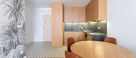 Una cocina moderna con armarios de madera, encimera de mármol y comedor con mesa y sillas de madera.