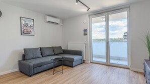 Una sala de estar moderna con un sofá seccional gris, una mesita redonda y vista al mar a través de una puerta corrediza de vidrio.