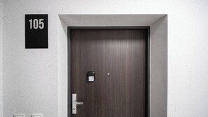 Una puerta de madera oscura con una cerradura digital y una llave, un letrero con el número '105' arriba y dos interruptores blancos en la pared.