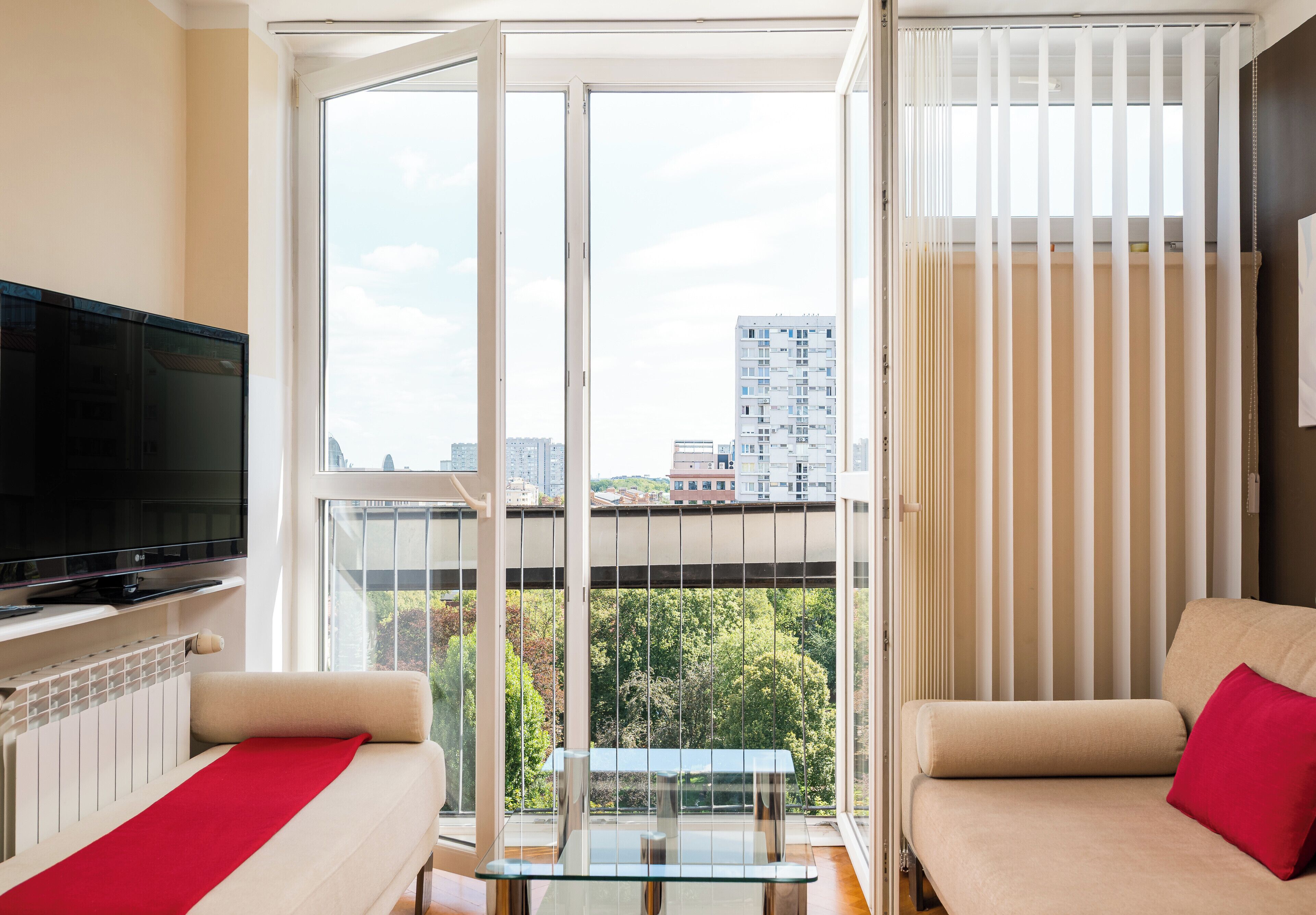 A modern living room with a large window, a flat-screen TV, and two sofas with red cushions.