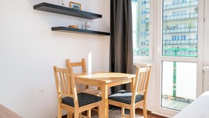 Una stanza con un tavolo e sedie in legno, una finestra che si affaccia su edifici e due mensole con oggetti decorativi.