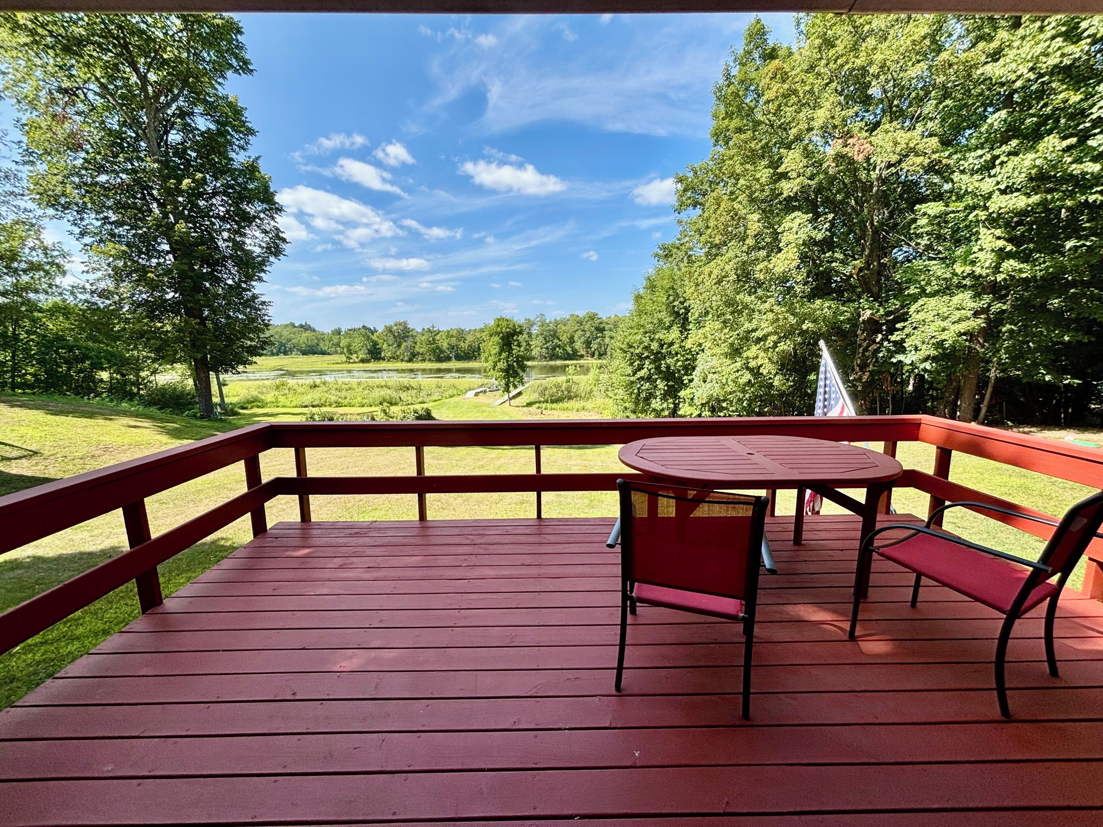 A wooden deck with a table and chairs, overlooking a grassy field and trees.