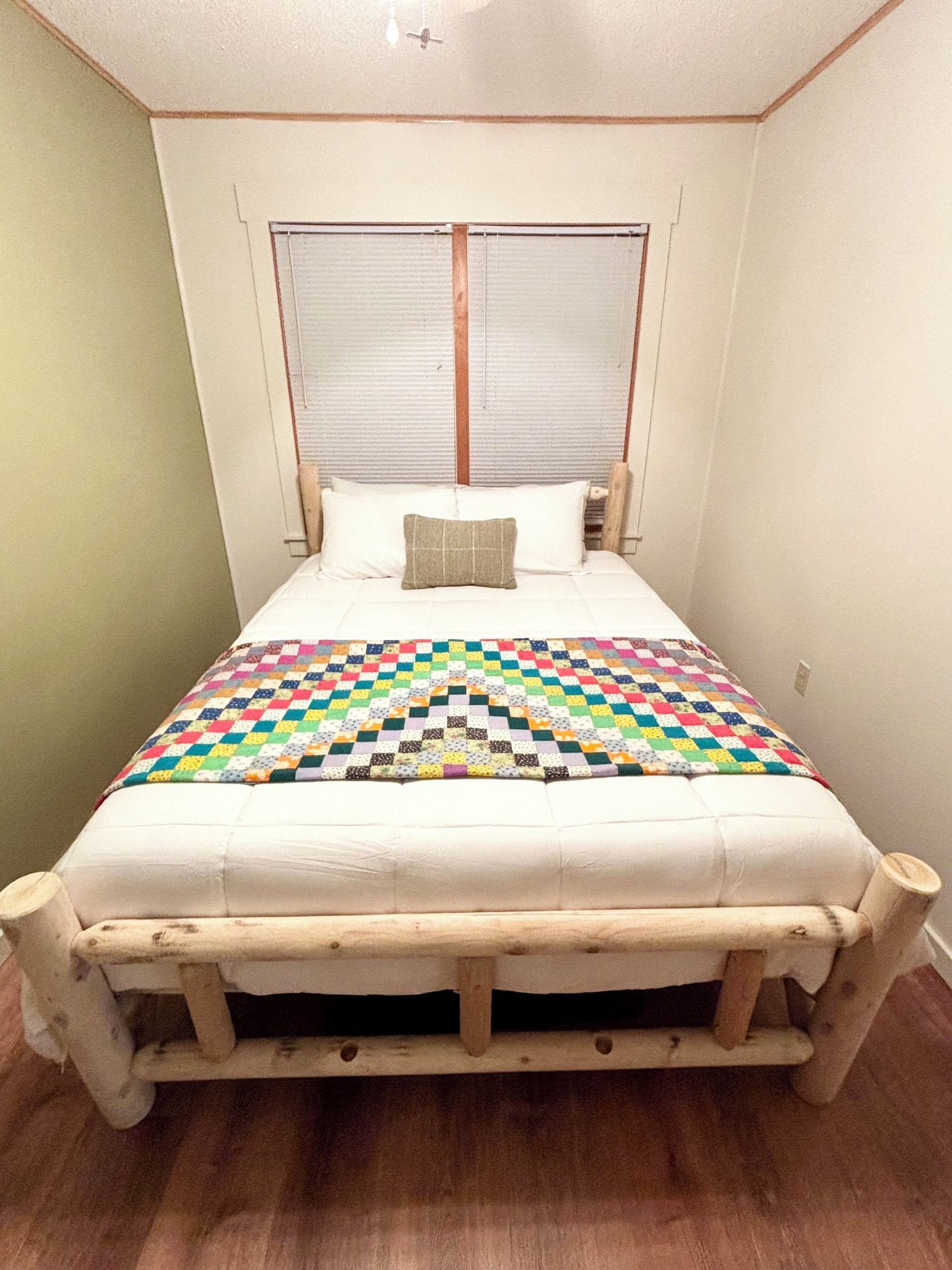 A bed with a wooden frame and a colorful quilt, a pillow, and a window with blinds.