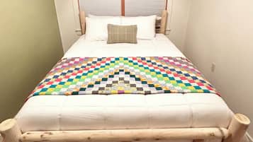 A bed with a wooden frame and a colorful quilt, a pillow, and a window with blinds.