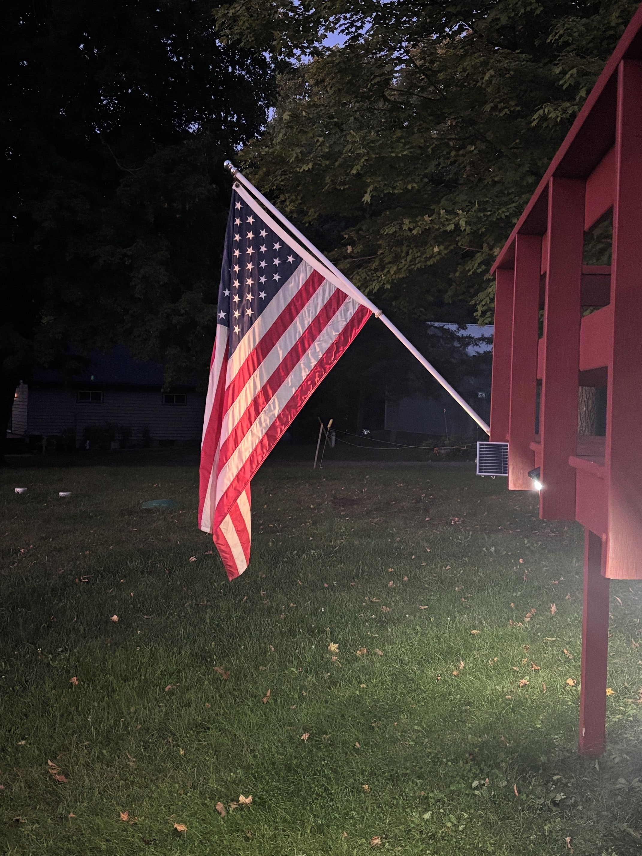 An American flag mounted on a flagpole in front of a red building.
